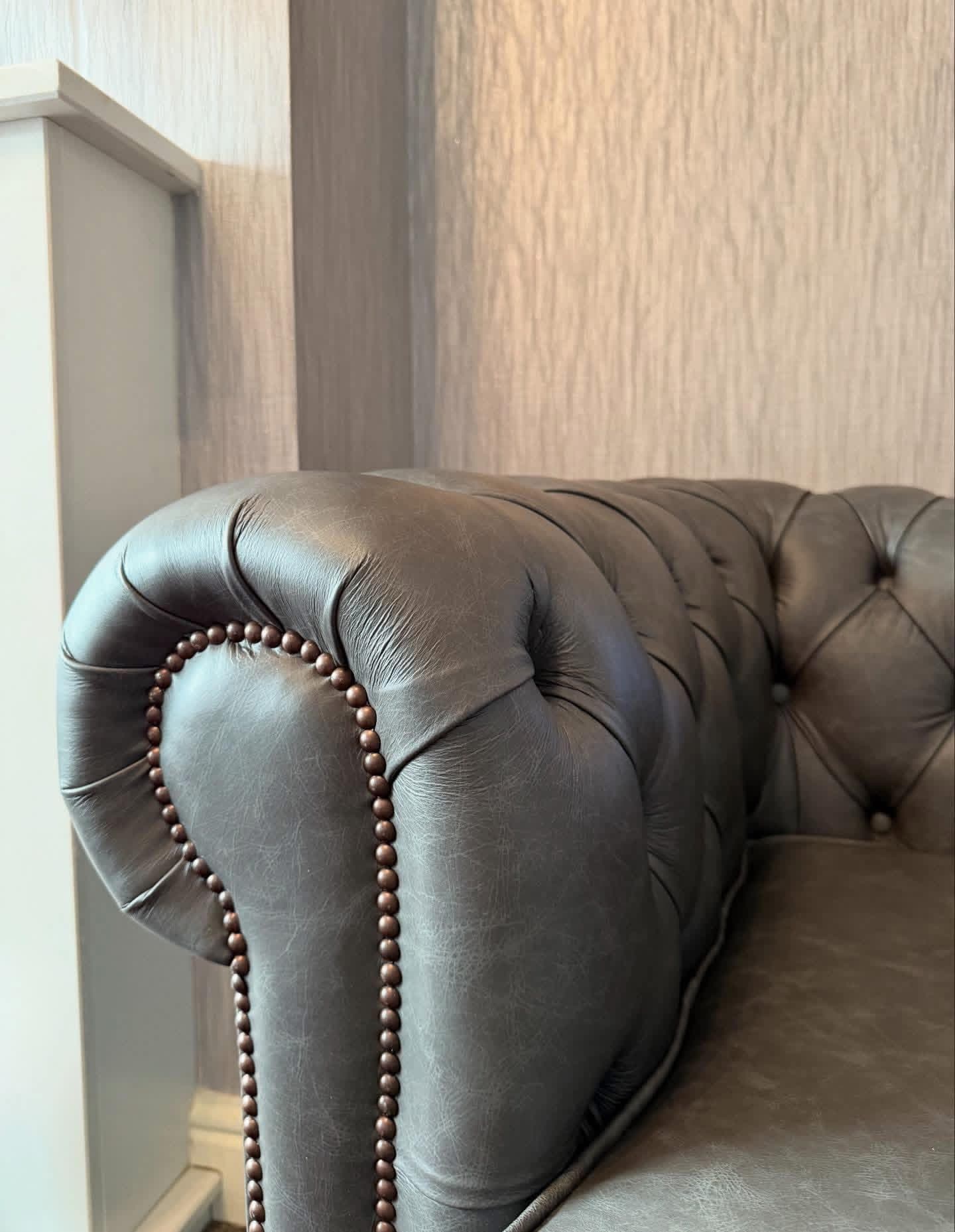 Close-up detail of hand-tufted leather sofa arm with brass nailhead trim
